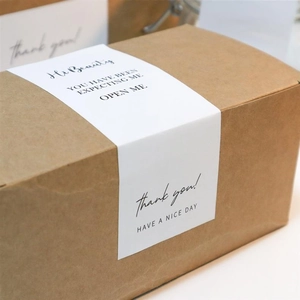 Macro shot of white rectangular packaging seals with black typography on kraft paper boxes
