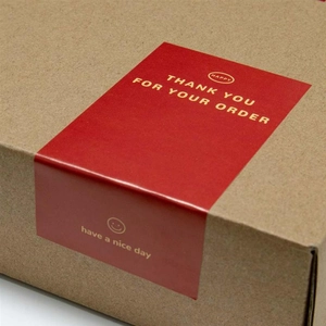 Detail of red rectangular Thank You stickers with smiley icon on a brown package box