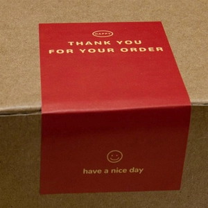 Macro shot of red rectangular Thank You stickers with smiley face on a cardboard box