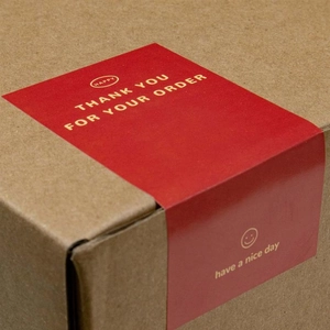 Detail of red rectangular Thank You seal stickers on a kraft shipping box corner