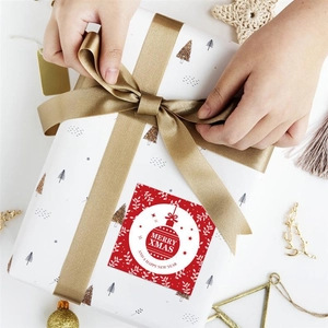 Close-up of red square Merry Xmas gift stickers being applied to a white gift box