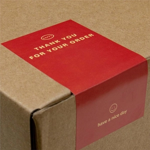 Red rectangular Thank You stickers with gold lettering on a brown corrugated box
