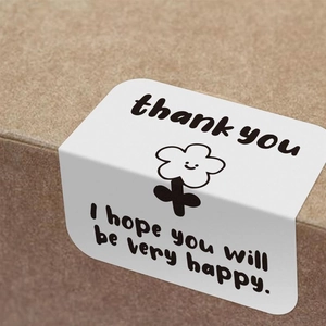 Close-up of rectangular 'Thank You' sealing sticker with smiling flower on a box