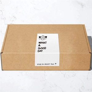 Brown kraft packaging box with What a Good Day decorative sticker on marble background