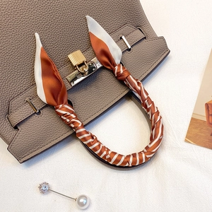 Détail d'un twilly en soie rayé orange noué sur une poignée de sac avec cadenas doré chic