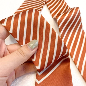 Gros plan du foulard en satin à rayures orange et blanc, texture douce et fini brillant