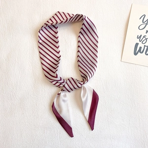 Détail d'un foulard en soie à rayures bordeaux et crème noué sur un tissu blanc texturé