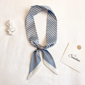 Détail d'un foulard en soie rayé bleu et blanc avec un fermoir à anneau perlé doré