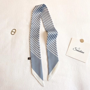 Gros plan d'un foulard en soie rayé bleu et blanc avec boucle dorée en D sur tissu blanc