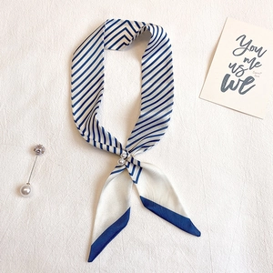 Détail de foulard en soie à rayures bleues avec boucles de perles sur tissu blanc texturé