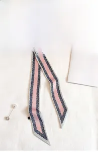 Dettaglio di una sciarpa twilly paisley rosa e blu navy con una spilla di perle e strass