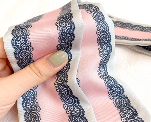 Dettaglio di un foulard in seta a righe rosa e bianche con motivi in pizzo nero
