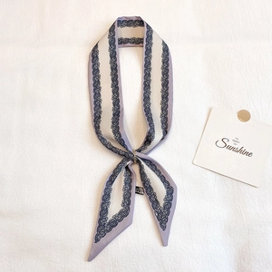 Dettaglio di sciarpa in seta lavanda con stampe in pizzo e anello di fissaggio in metallo oro