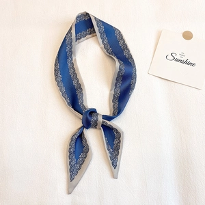 Dettaglio di una sciarpa di seta blu con stampa paisley annodata su tessuto bianco testurizzato