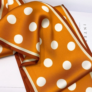 Detailed close-up of orange polka dot silk scarf with elegant contrast border texture