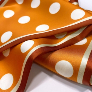 Macro shot of orange silk scarf with white polka dots showing satin texture and draping