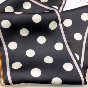 Close-up of black polka dot silk scarf with pink edges and smooth satin texture