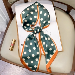 Close-up of silk-feel dark green polka dot scarf with contrasting orange hem on a magazine