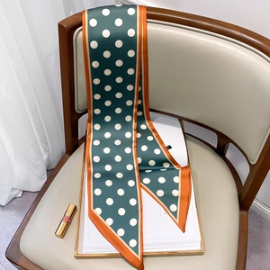 Detail of dark green polka dot silk scarf with orange borders on a beige chair