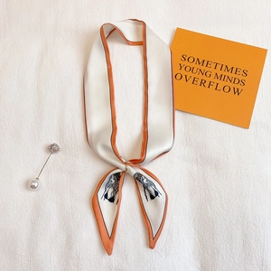 Détail d'une écharpe en soie ivoire étroite avec bordure orange, anneau doré et broche
