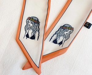 Détail d'un foulard twilly fin avec illustration de portrait et bords roulés orange