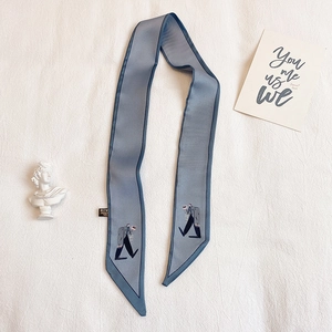 Détail d'un foulard étroit bleu-gris avec illustration de figurine et ourlet bleu foncé