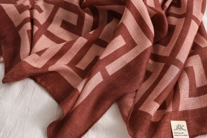 Detail of burgundy geometric Greek key pattern scarf with woven brand label and linen texture