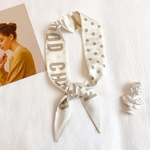 Elegant long polka dot and letter print silk scarf tied in a knot on a white background