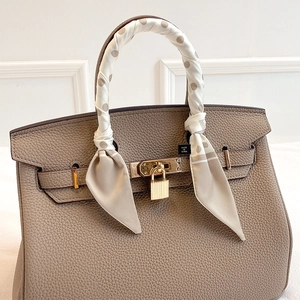 Polka dot silk scarf tied on an elephant gray lychee leather handbag with gold padlock