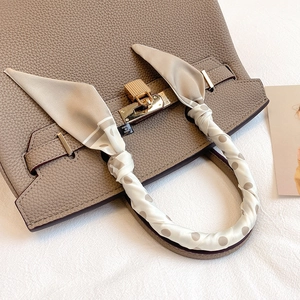 Close-up of brown pebbled leather handbag with gold lock and polka dot silk scarf handle