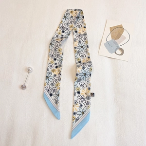 Nahaufnahme eines Seidenschals mit Gänseblümchen-Print und blauem Rand auf weichem Stoff