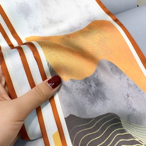 Detailed close-up of soft silk-like scarf featuring orange mountain print and stripe edge