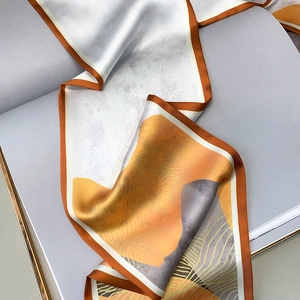 Detail of a luxury narrow silk twilly scarf with abstract orange and grey geometric patterns