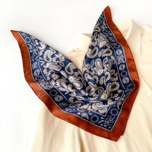 Close-up of a navy silk scarf with paisley patterns and a contrast brick red border