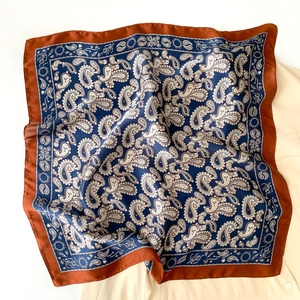 Close-up of square silk scarf with blue paisley pattern and contrast red borders