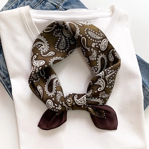 Close-up of a green paisley silk scarf tied in a neat knot on a white T-shirt neckline
