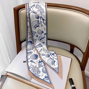Detail eines weißen Seidenschals mit blauem Ozeanmuster auf einem beigen Stuhl