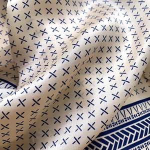 Detailed macro view of cream silk scarf with blue cross pattern and satin texture