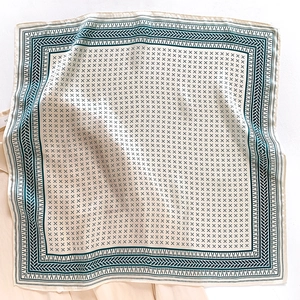 Detail of silk square scarf featuring dark green geometric patterns and ivory texture