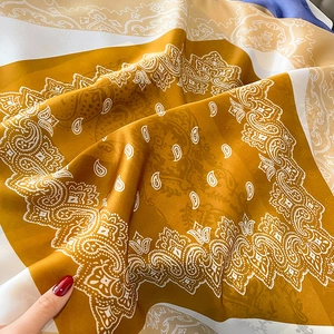 Detailopname van zijdezachte mosterdgele sjaal met wit paisley patroon en elegante plooien