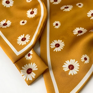 Detailed close-up of mustard yellow satin scarf with white daisy floral prints and silky texture