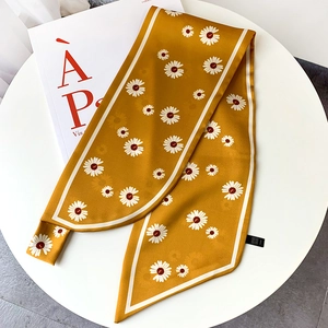 Detailed view of yellow silk scarf with white daisy print on a minimalist white desk