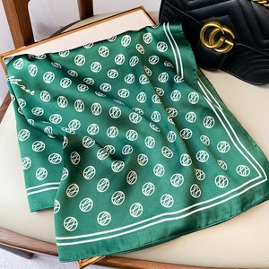 Detail of emerald green silk scarf with white abstract patterns and Monet lettering
