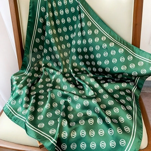 Detail of forest green silk scarf with white geometric patterns on a wooden chair