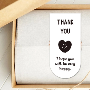 U-shaped white thank you sticker with smiling heart on a brown gift box packing