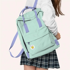 Detail of mint green nylon backpack with purple straps and smiley face medal on pink background