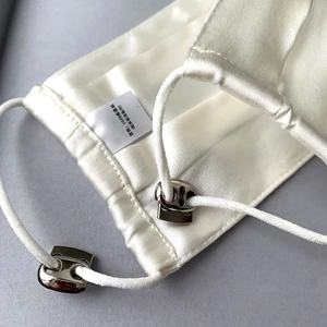 Detail of white silk face mask featuring adjustable elastic ear loops with metal buckles