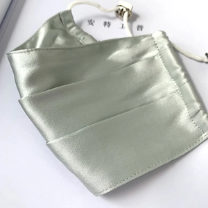 Detail of light green silk face mask with adjustable white ear loops and soft satin sheen