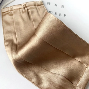 Macro view of champagne silk face mask with elegant pleats and elastic ear loops
