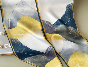 Dettaglio ravvicinato di foulard in raso con motivi astratti di montagna e spilla di perle